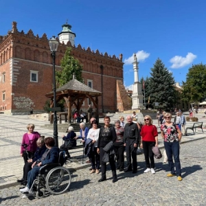 Fotografia przedstawia grupowe ujęcie seniorów DDS+ na Rynku Starego Miasta w Sandomierzu